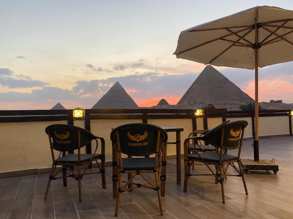 2 sillas y una sombrilla en un balcón con pirámides en Pyramids Era View en El Cairo