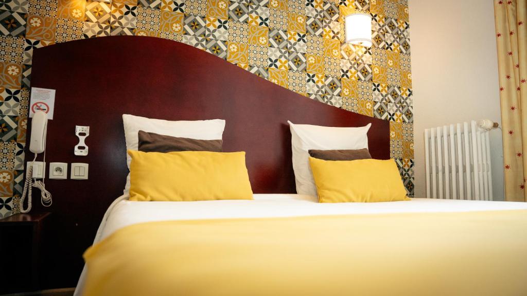 a bedroom with a large bed with yellow pillows at Hotel les Commercants in Clermont-Ferrand