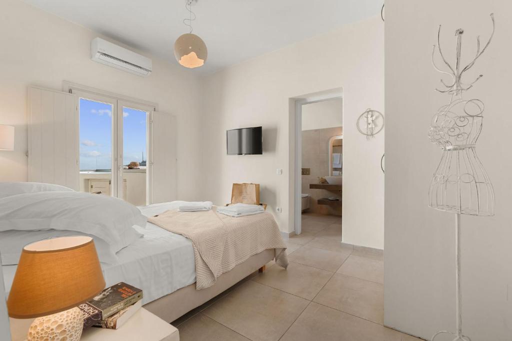 a white bedroom with a bed and a tv at Lithos Houses in Pyrgos