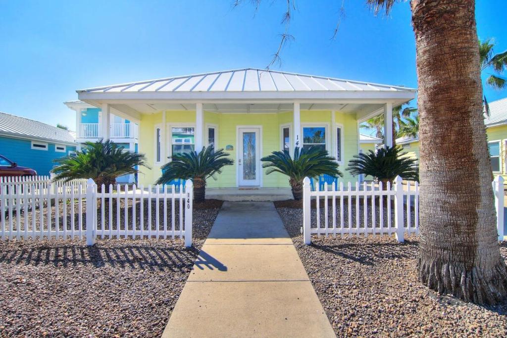 une maison jaune avec une clôture blanche et des palmiers dans l'établissement Tropical Niche at Royal Sands, à Port Aransas