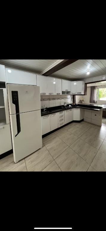 a large kitchen with white cabinets and a refrigerator at Casa Inteira com Churrasqueira in Ponta Grossa