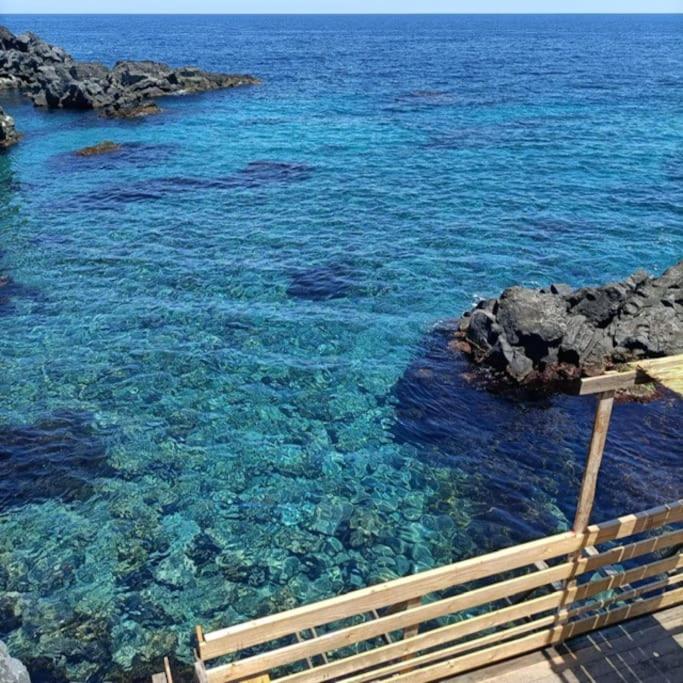 um corpo de água com pedras e água azul em The Bays - La Mansarda ad un passo dal mare em Acireale