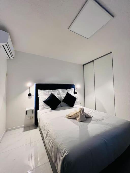 um quarto branco com uma cama grande e almofadas pretas em T1 - Le Papangue 5* - neuf, vue jardin, 8’ airport em Sainte-Clotilde
