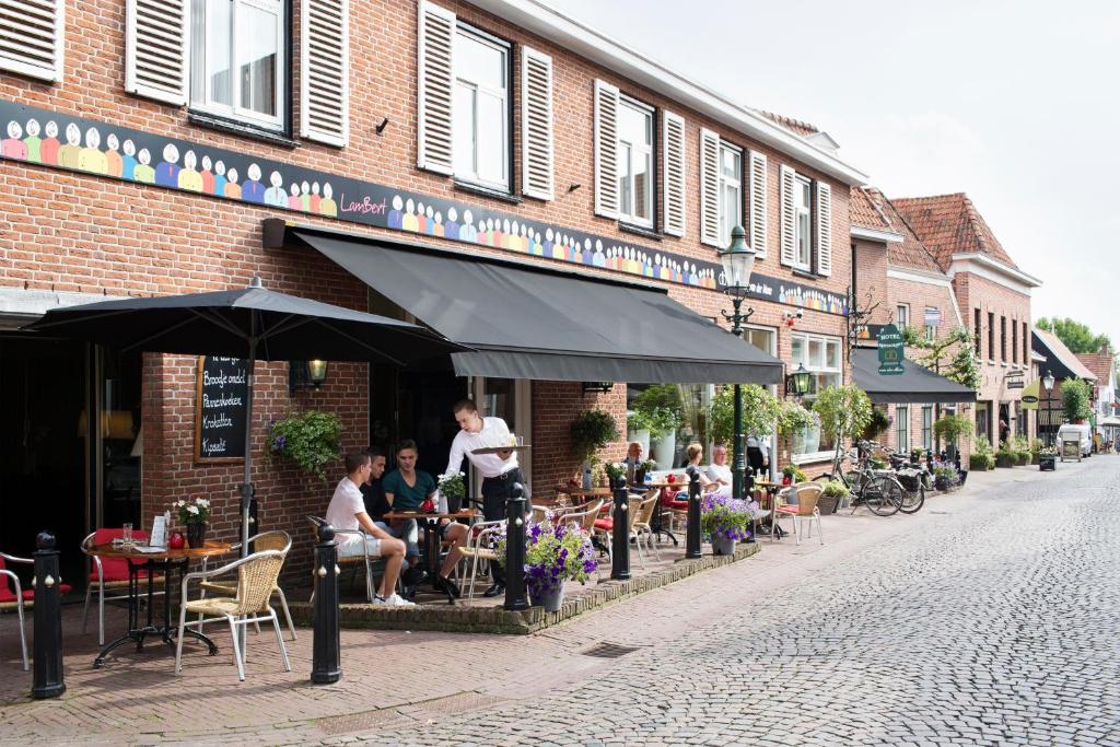 een groep mensen die aan tafels buiten een gebouw zitten bij Hotel Van der Maas in Ootmarsum