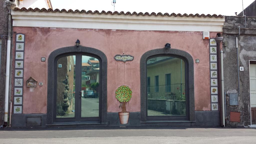 un bâtiment rose avec deux grandes fenêtres et une plante en pot dans l'établissement Oltre Il Giardino, à Pedara