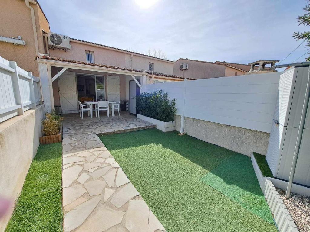 une cour avec une clôture blanche et de l'herbe verte dans l'établissement Maison mitoyenne climatisée avec piscine, grande terrasse, proche plage à Marseillan - FR-1-326-809, à Marseillan