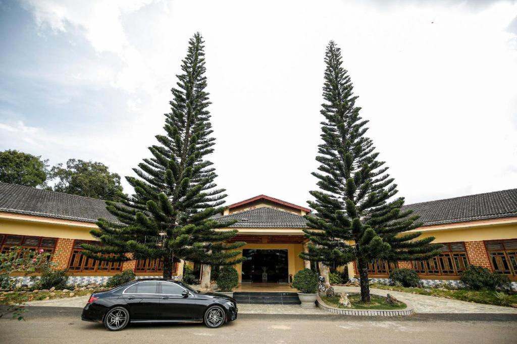 samochód zaparkowany przed budynkiem z dwoma drzewami w obiekcie Resort Dakke Măng Đen w mieście Kon Von Kla