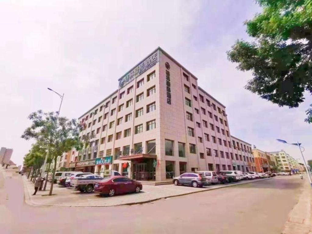 duży budynek przy ulicy miejskiej z zaparkowanymi samochodami w obiekcie Green Tree Inn Wuzhong Litong District High-Speed Railway Station w mieście Wuzhong