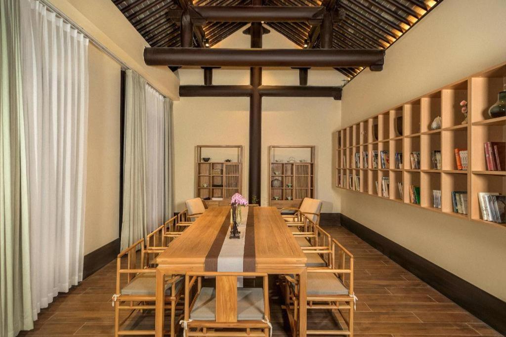 a long wooden table with chairs in a library at Blossom House Xuzhou Huilongwo Banyunting in Xuzhou