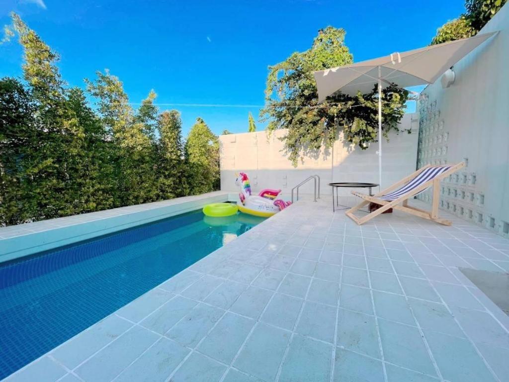 a swimming pool with a chair and an umbrella at 7 Class Pool Villa in Chachoengsao