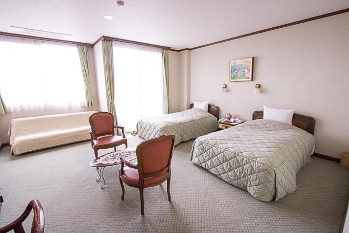 1 dormitorio con 2 camas, sillas y ventana en ホテル中山荘, en Miyakonojō