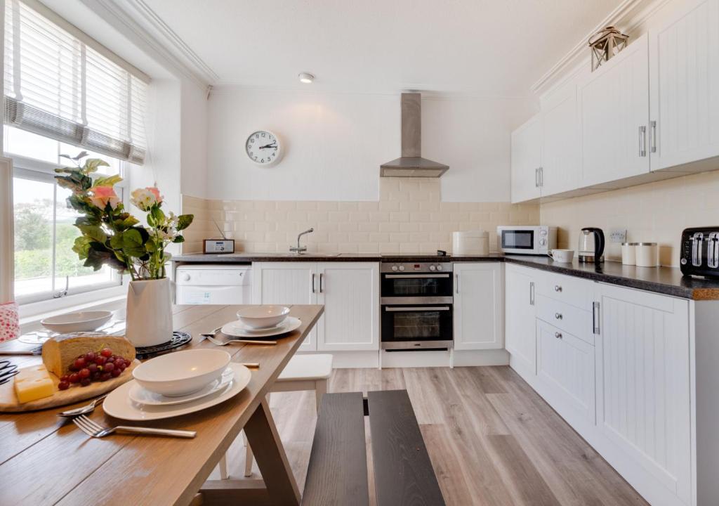 a kitchen with white cabinets and a wooden table at Bronwydd in Abersoch
