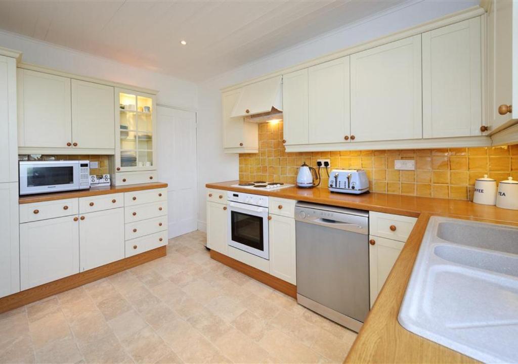 a large kitchen with white cabinets and a sink at Wendon in Abersoch