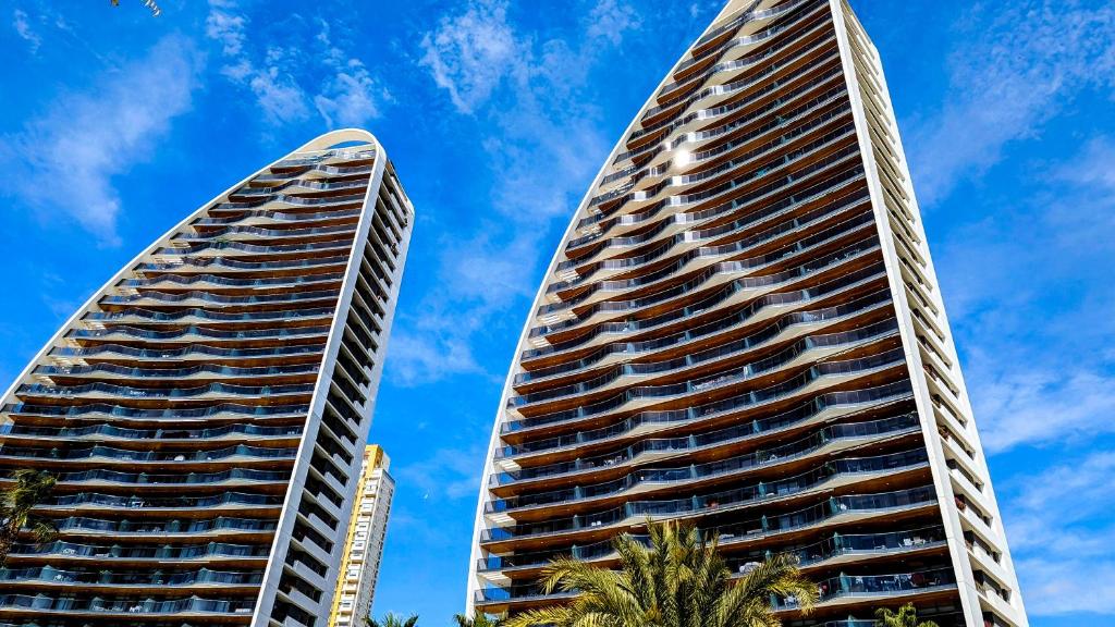 two tall buildings with palm trees in front of a blue sky at SUNSET WAVES luxury apartment in Benidorm