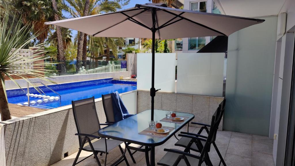 een tafel en stoelen met een parasol naast een zwembad bij MIRADOR Poniente beach apartments in Benidorm