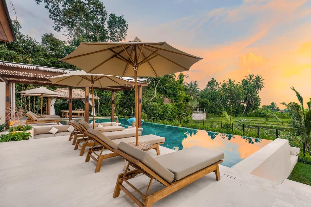 een groep stoelen en parasols naast een zwembad bij Villa Rosita by BaliSuperHost in Ubud