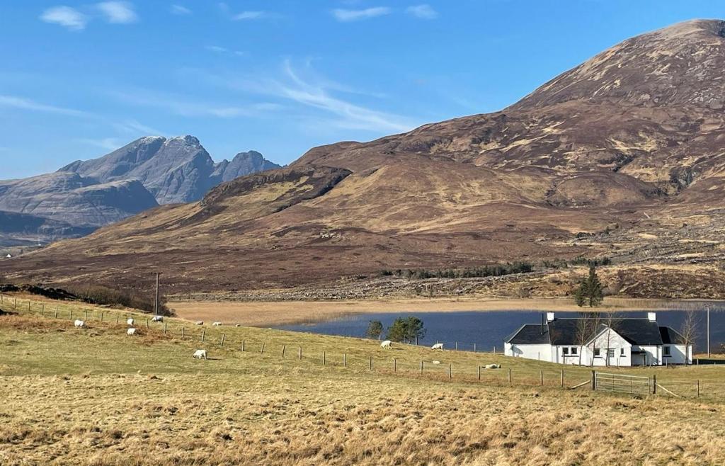 a house in a field next to a mountain at Taigh Cill Chriosd in Kilbride