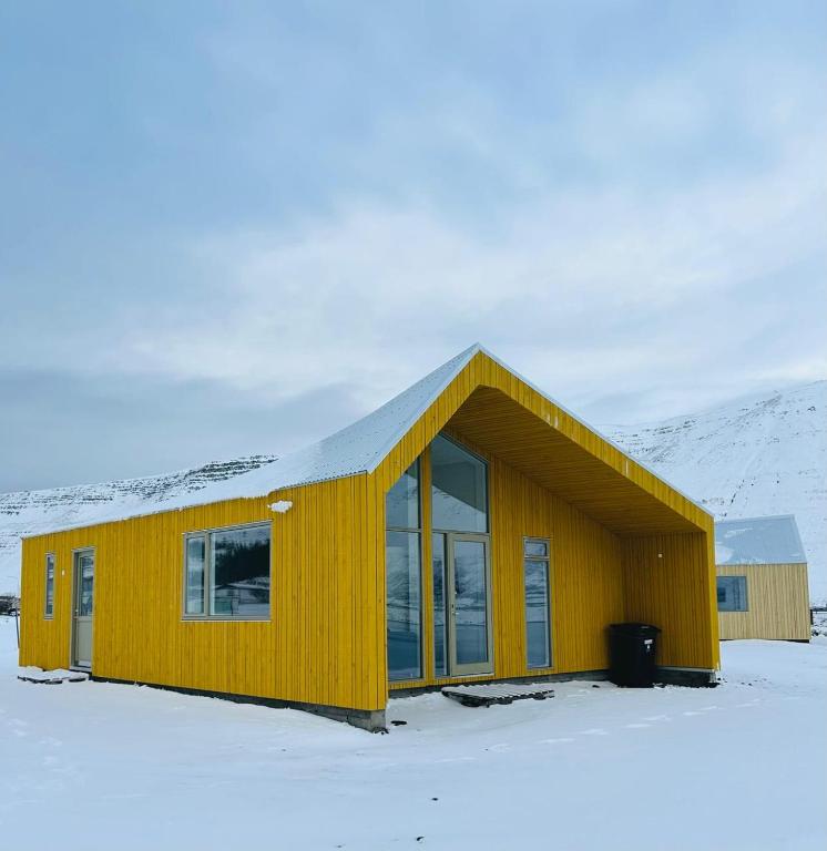 een geel huis in de sneeuw met een berg bij Fisk Club Cottages in Suðureyri