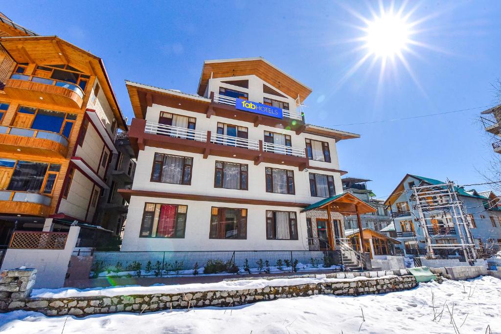 a building in the snow with the sun behind it at FabHotel Manali Heaven in Manāli