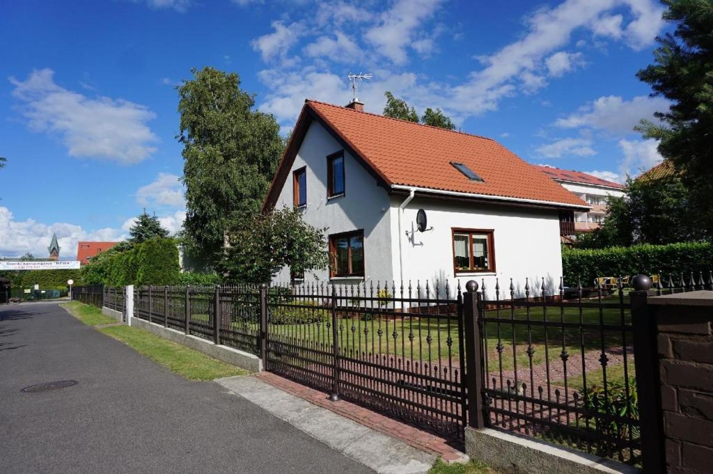 a white house with a red roof behind a fence at Ferienhaus für 4 Personen und 2 Kinder in Ustronie Morskie, Ostseeküste Polen in Ustronie Morskie