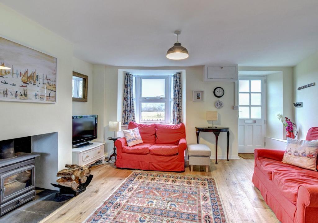 a living room with two red couches and a television at Meadow Cottage in Bridport