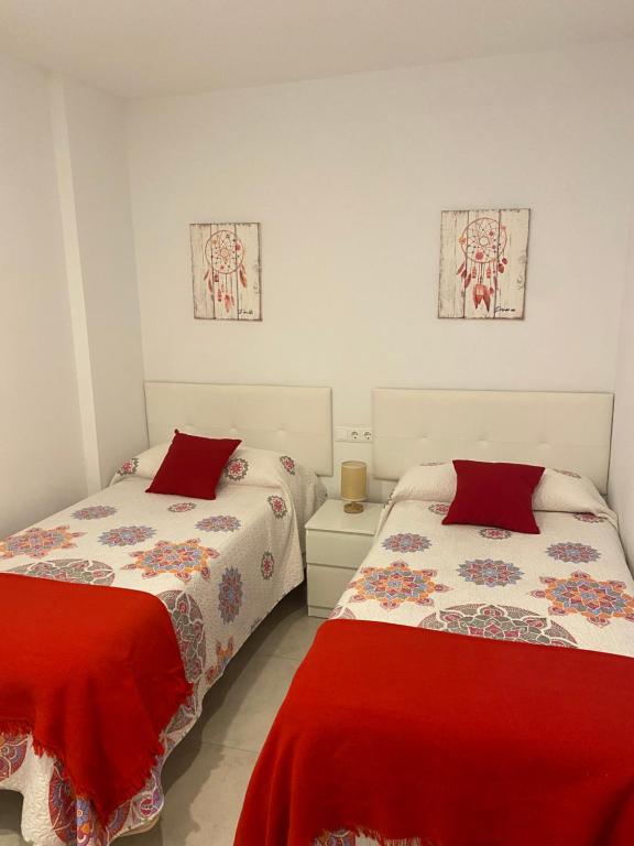 two beds in a white room with red sheets at TURISMO LOS LANCES TARIFA( PARKING GRATUITO) in Tarifa