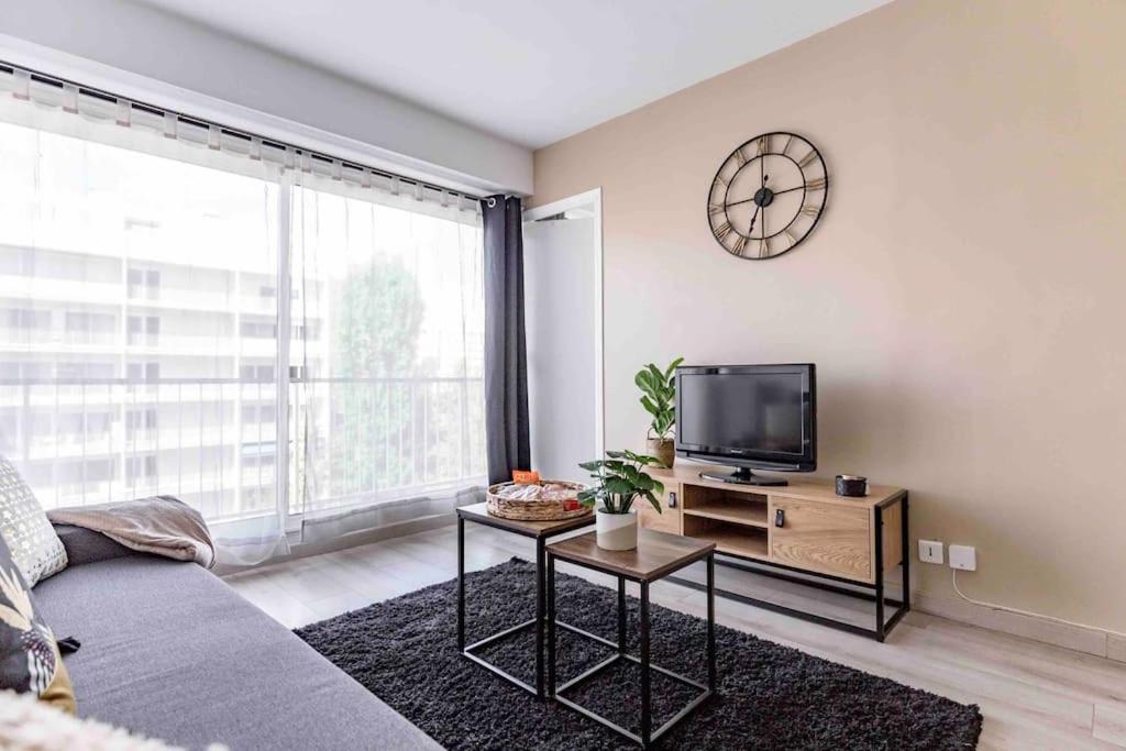 een woonkamer met een bank, een tv en een klok bij Appartement avec parking et terrasse Métro 7 et Paris in Villejuif