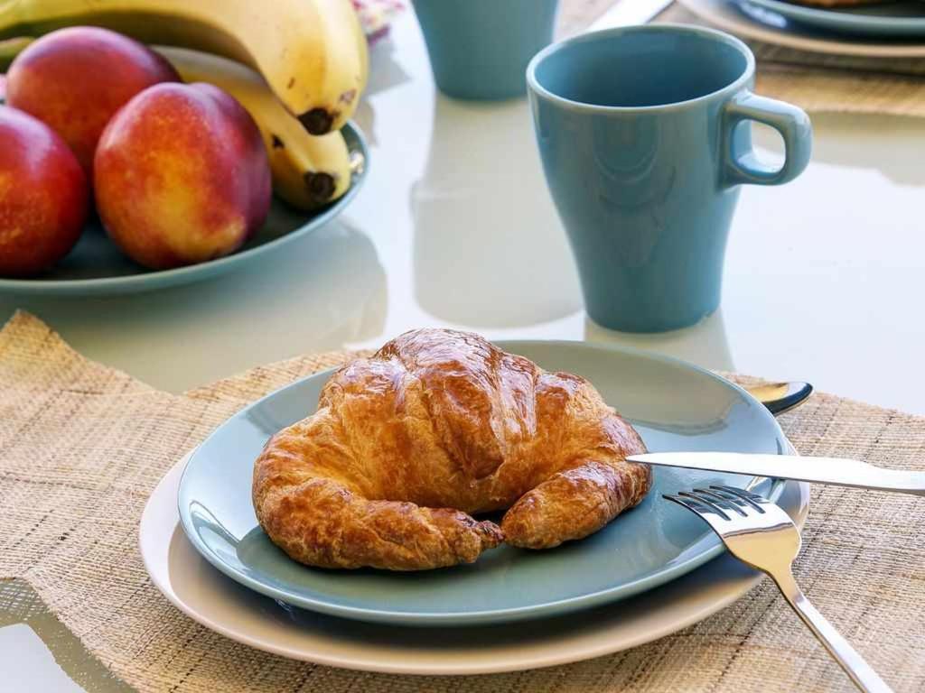 a plate with a croissant on a table with a cup of fruit at Gardenias de playa gandia in Puerto de Gandía