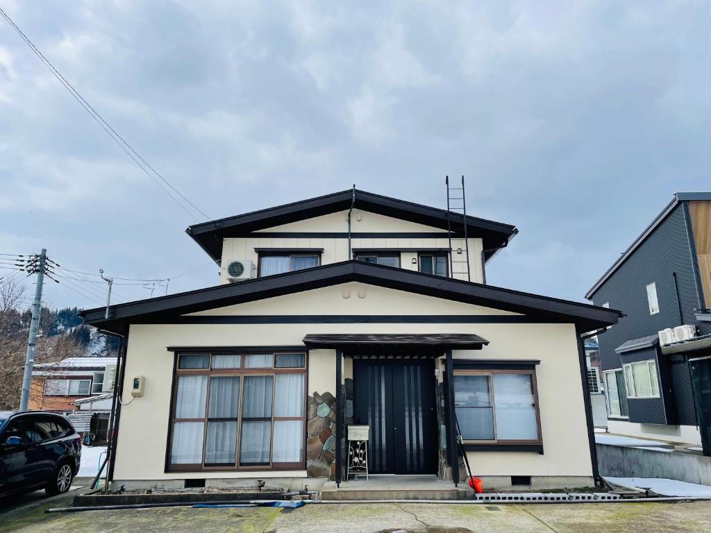 uma casa branca com um telhado preto em Urasa Cottage @ Snow Countryside em Minami Uonuma