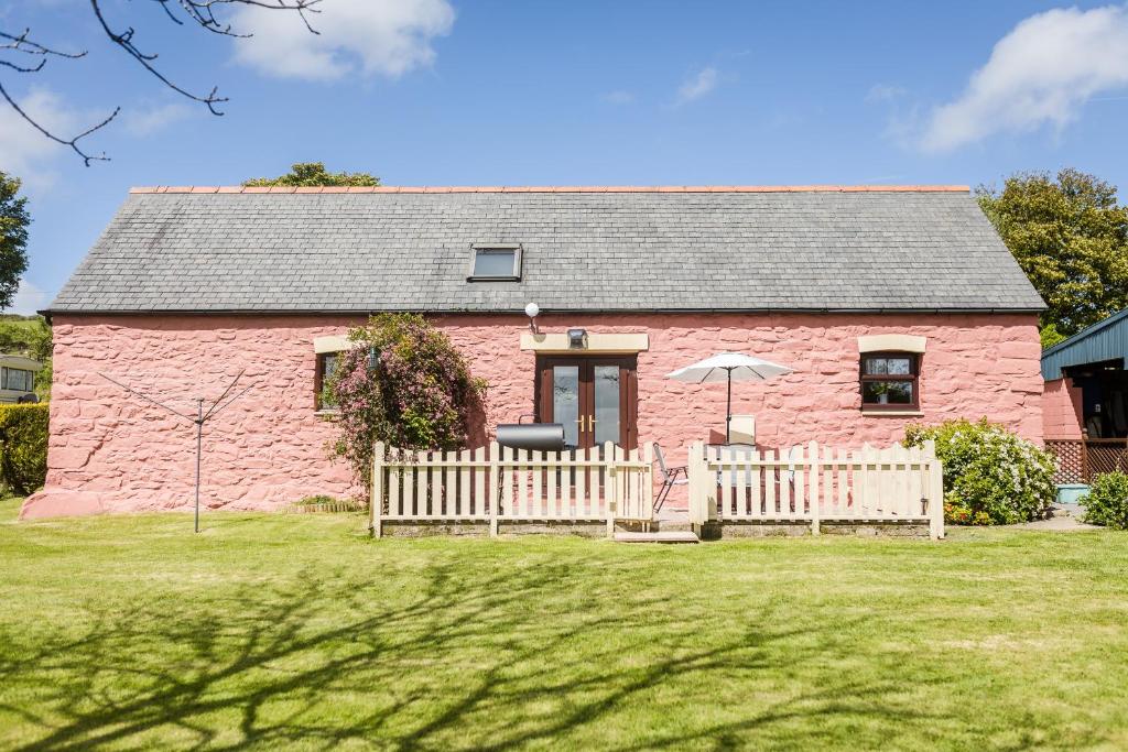 una casa de ladrillo rosa con una valla y una sombrilla en Meini Glas Mynachlogddu, en Mynachlogddu