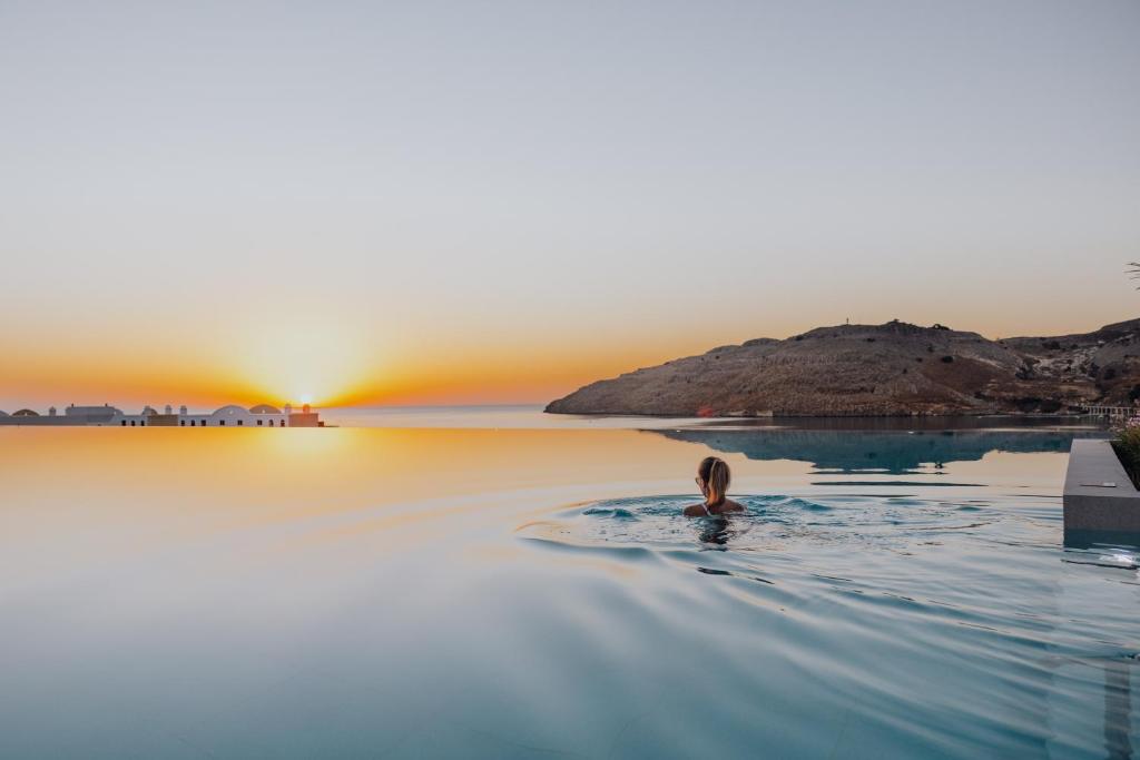 a woman swimming in the dead sea at sunset at Lindos Grand Resort & Spa - Adults Only in Líndos