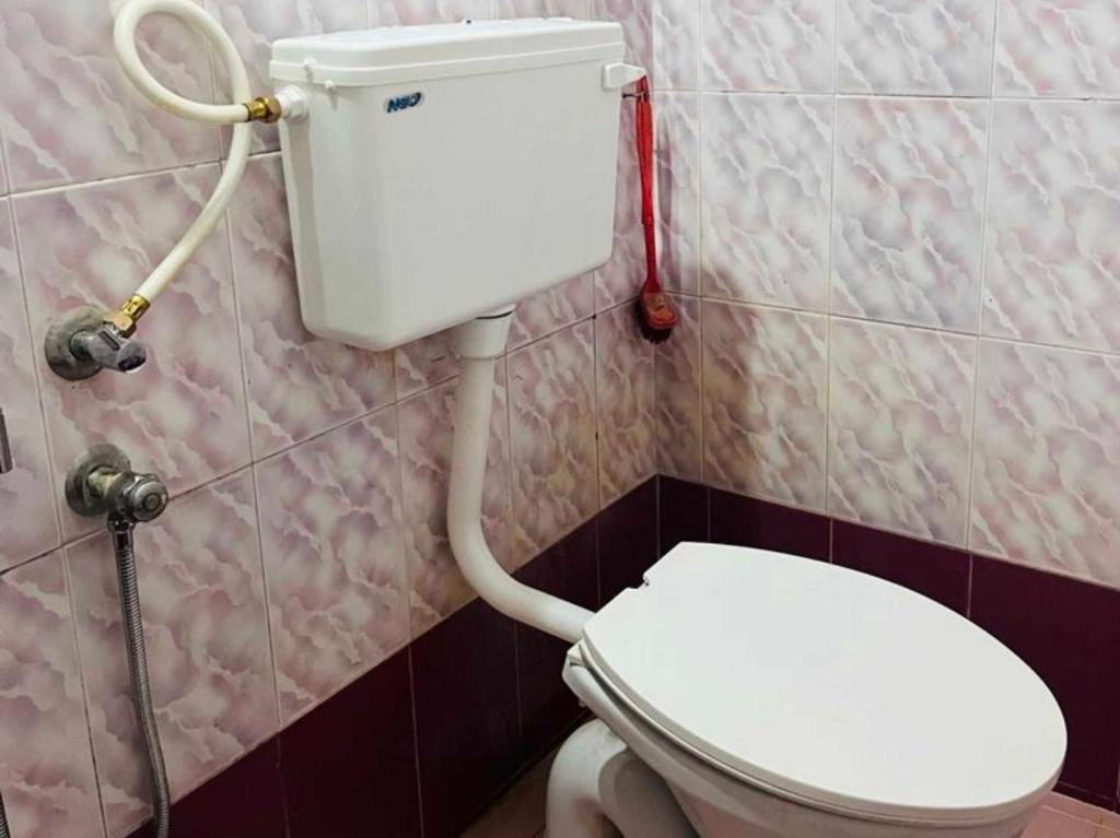 a bathroom with a white toilet in a room at OYO GoodInn Apartment in Elūr