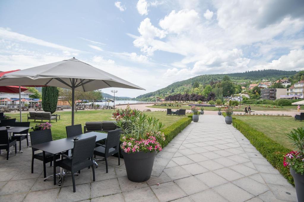 a patio with tables and chairs and an umbrella at Hôtel Beau Rivage in Gérardmer