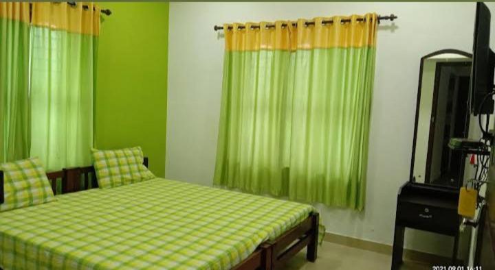 a bedroom with green curtains and a bed and a mirror at Heaven Homestay in Alleppey