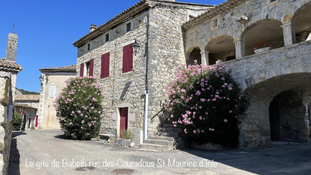a stone building with pink flowers in front of it at Le Gîte De Babeth in Saint-Maurice-dʼIbie