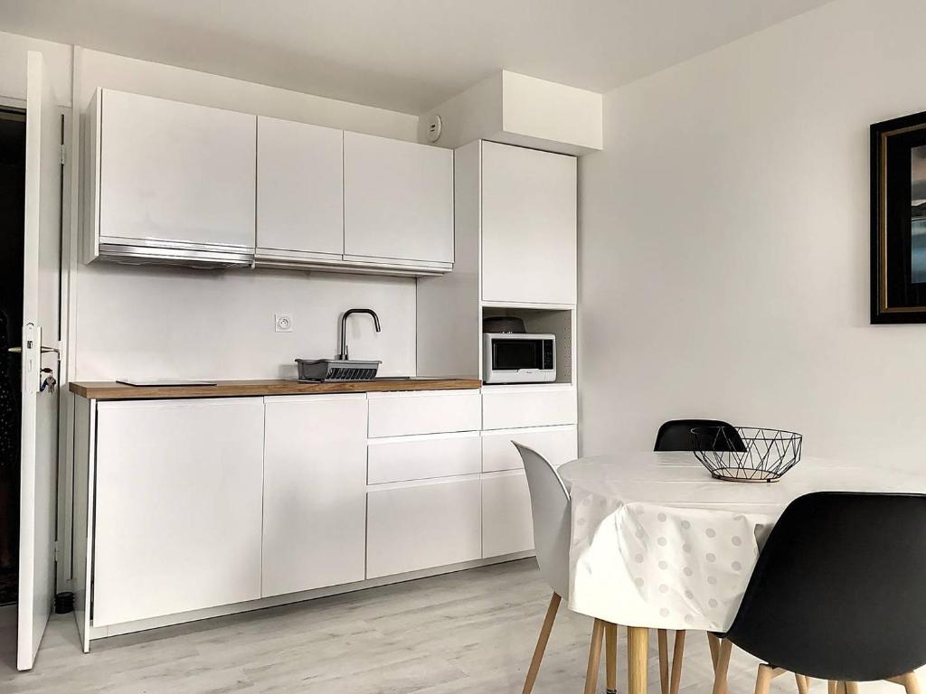 une cuisine avec des armoires blanches et une table avec des chaises dans l'établissement 106 - Appartement rénové Sables d'Or Les Pins, à Fréhel