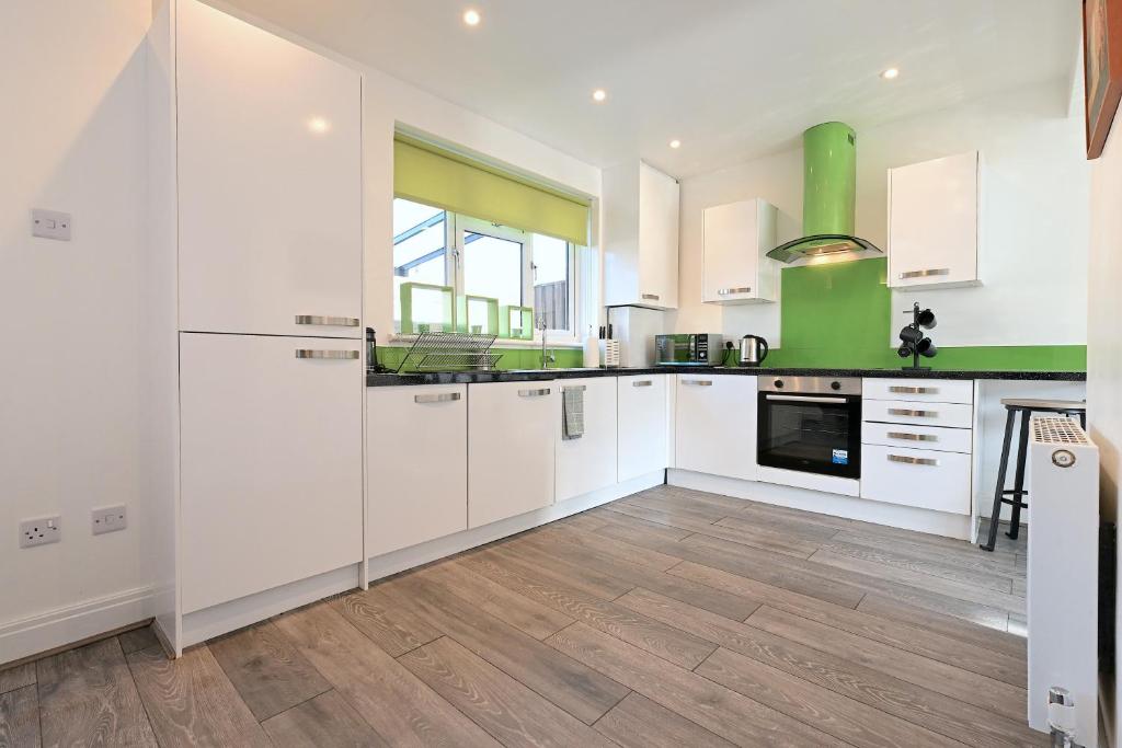 a kitchen with white cabinets and a green wall at Vibrant 3BD home with great links to the city in London