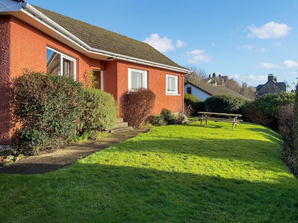 a house with a grassy yard next to a bench at Rhuside in Campbeltown