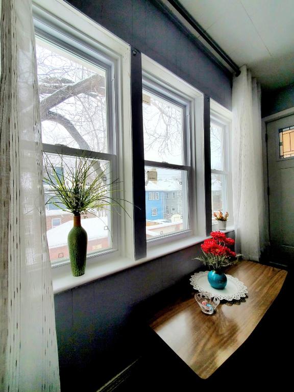 a room with two windows with flowers on a wooden table at Merj's Guest House in Wolesly in Winnipeg