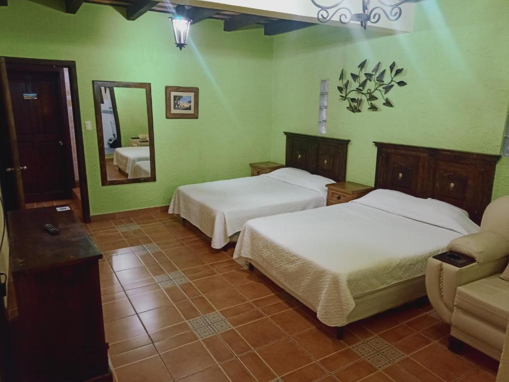 Hotel El Mirador Anexo 1 في Santa Lucía Milpas Altas: غرفة نوم بسريرين ومرآة وأريكة
