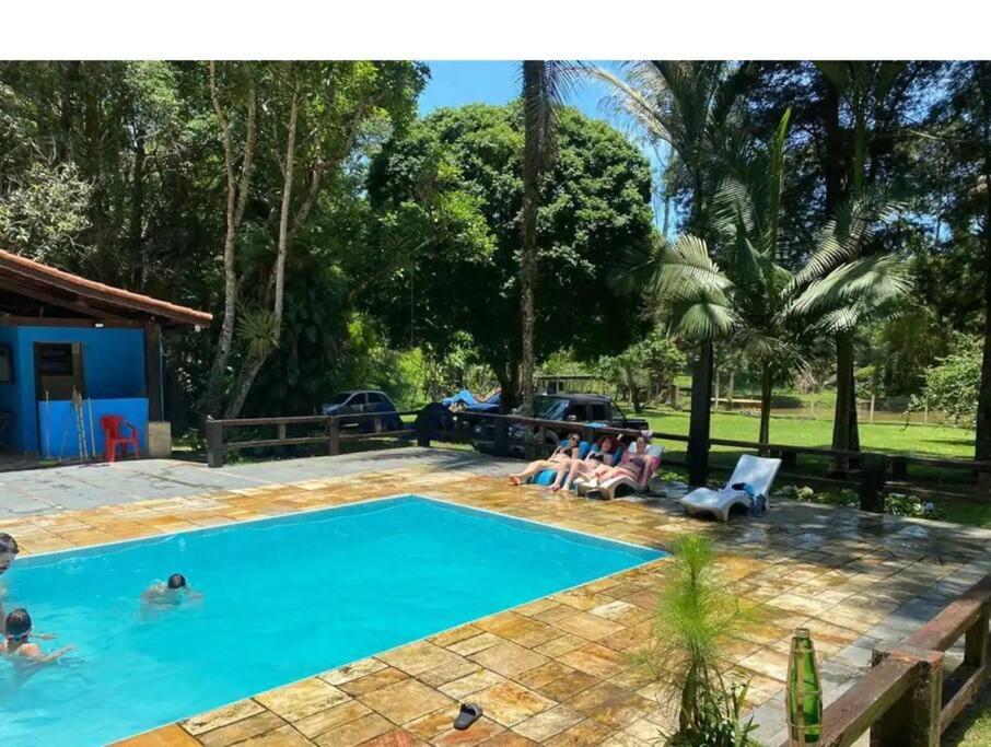 a group of people sitting around a swimming pool at Casa de campo agradável com piscina, parquinho, lago, riacho, quadra, sinuca e mais! in Juquitiba