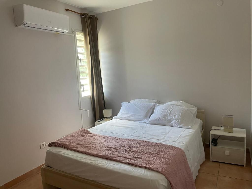 een slaapkamer met een bed met witte lakens en een raam bij Appartement BALISIER in Saint-François