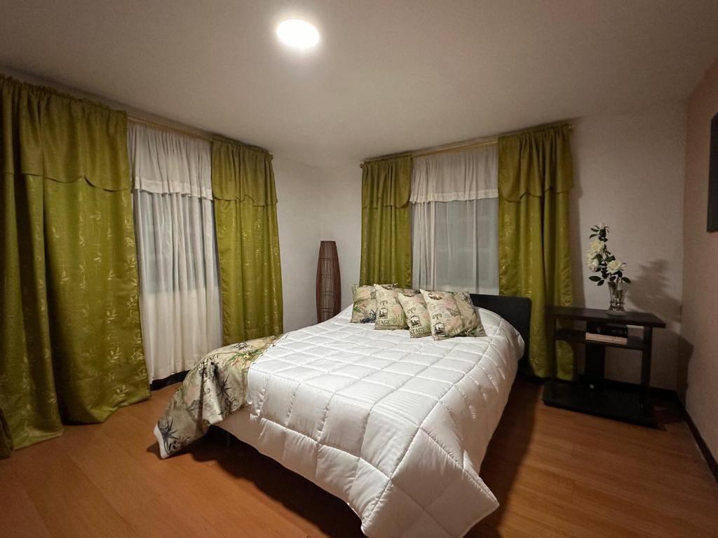 a bedroom with a white bed and green curtains at El Refugio del Colibrí in Santa Rosa de Cabal