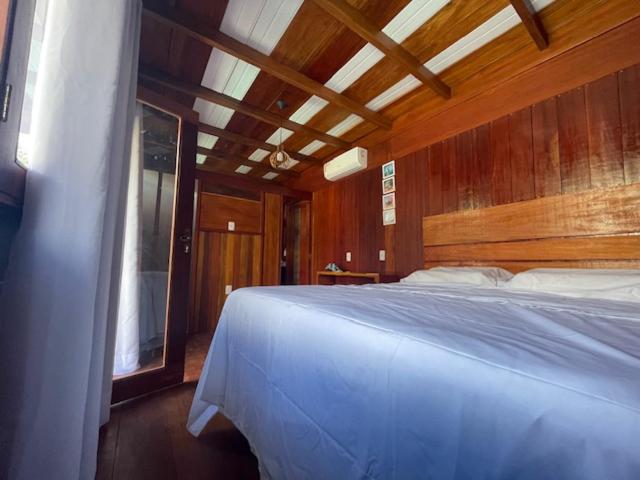 um quarto com uma cama branca e uma parede de madeira em Chalés Mãe Natureza em Vera Cruz de Itaparica