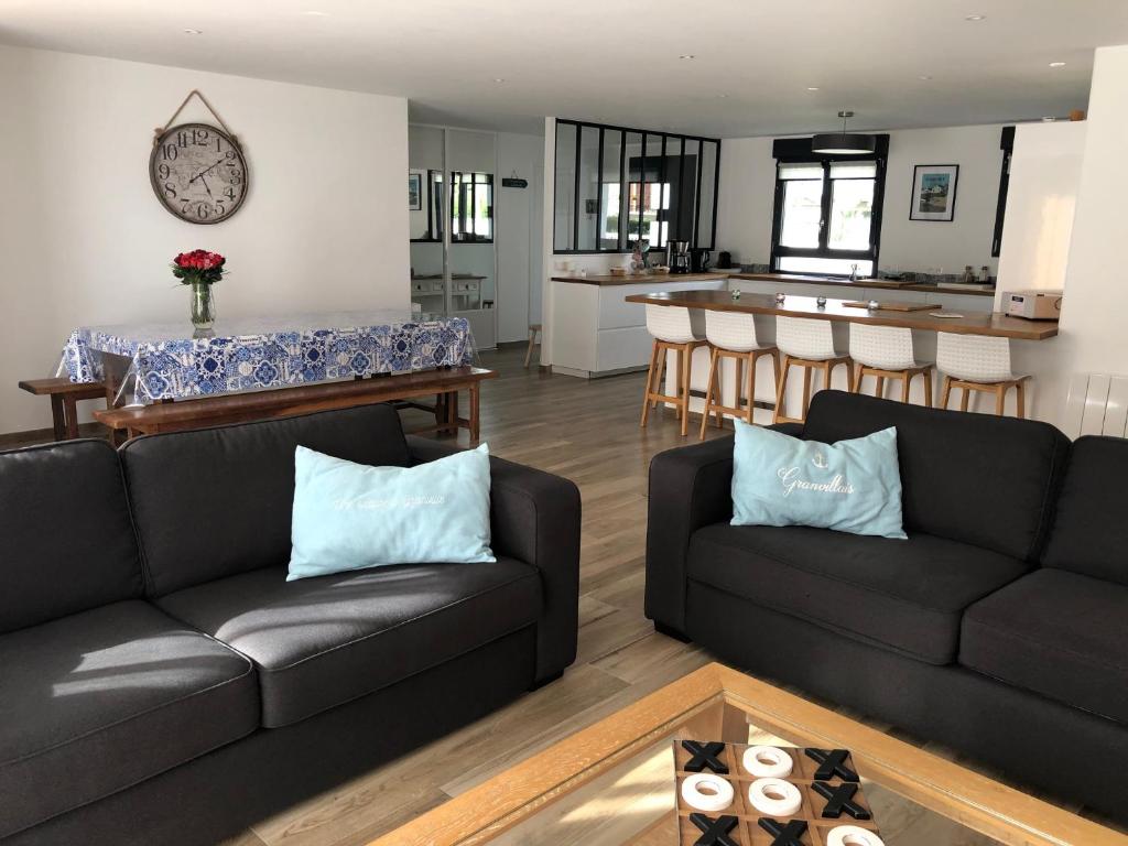 een woonkamer met twee zwarte banken en een keuken bij Maison proximité Golf et plage de Bréville sur Mer in Bréville-sur-Mer