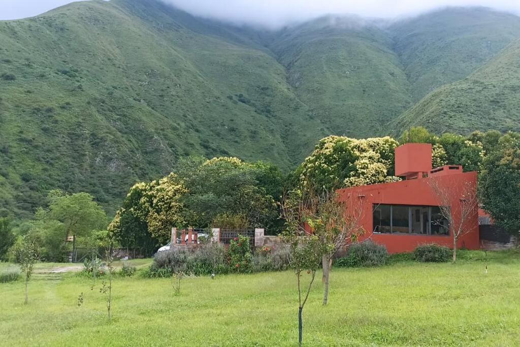 a red house in a field with mountains in the background at finca de barcena, country house in Tumbaya