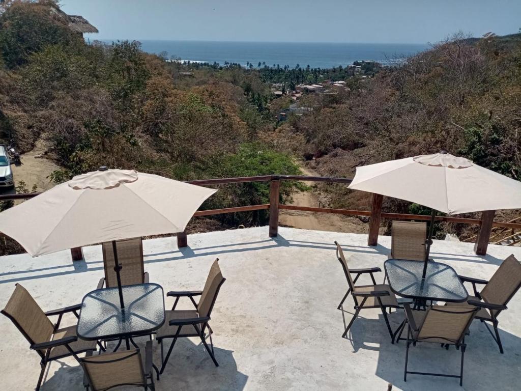 2 Tische und Stühle mit Sonnenschirmen auf einer Terrasse in der Unterkunft HOTEL AVE FENIX in Mazunte