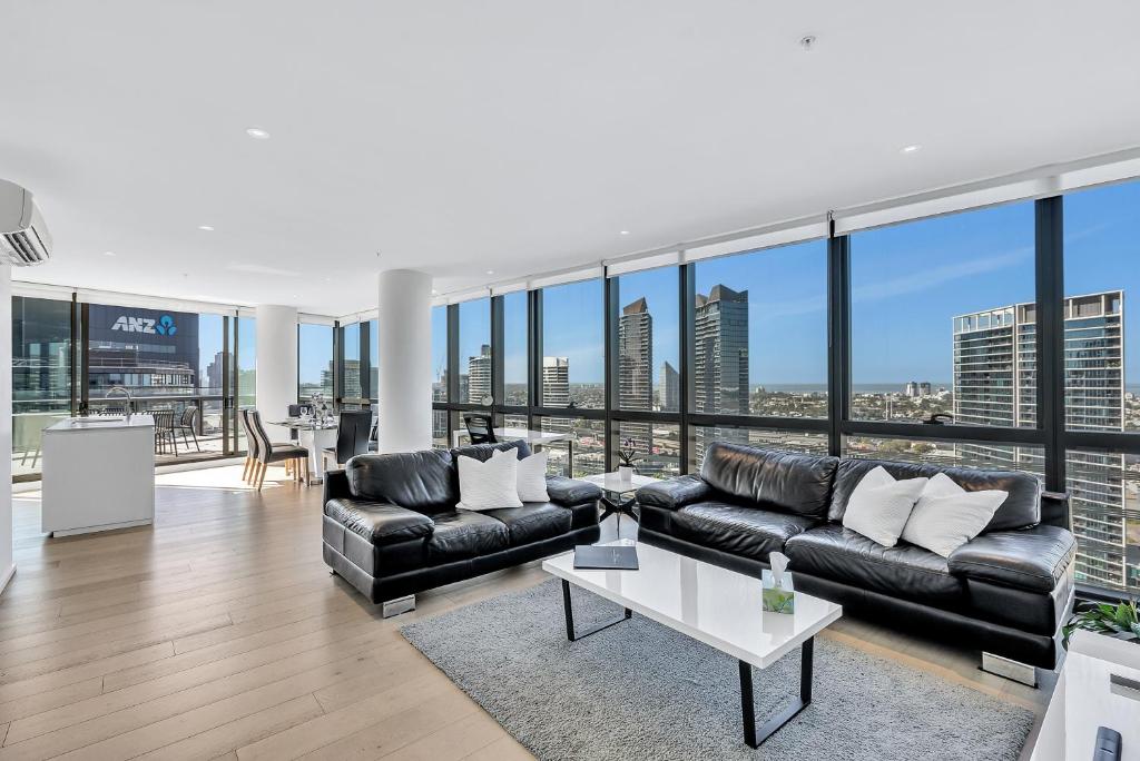 una sala de estar con muebles de cuero negro y ventanas grandes. en Melbourne Lifestyle Apartments – Best Views on Collins en Melbourne