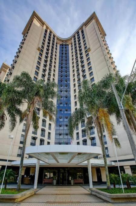 a large building with palm trees in front of it at Flat de Luxo Aeroporto Congonhas - Hotel in São Paulo