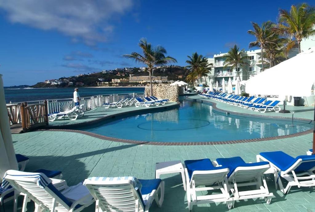 een zwembad met blauwe en witte stoelen en de oceaan bij Coral Beach Club Condo Dawn Beach condo in Upper Princeʼs Quarter